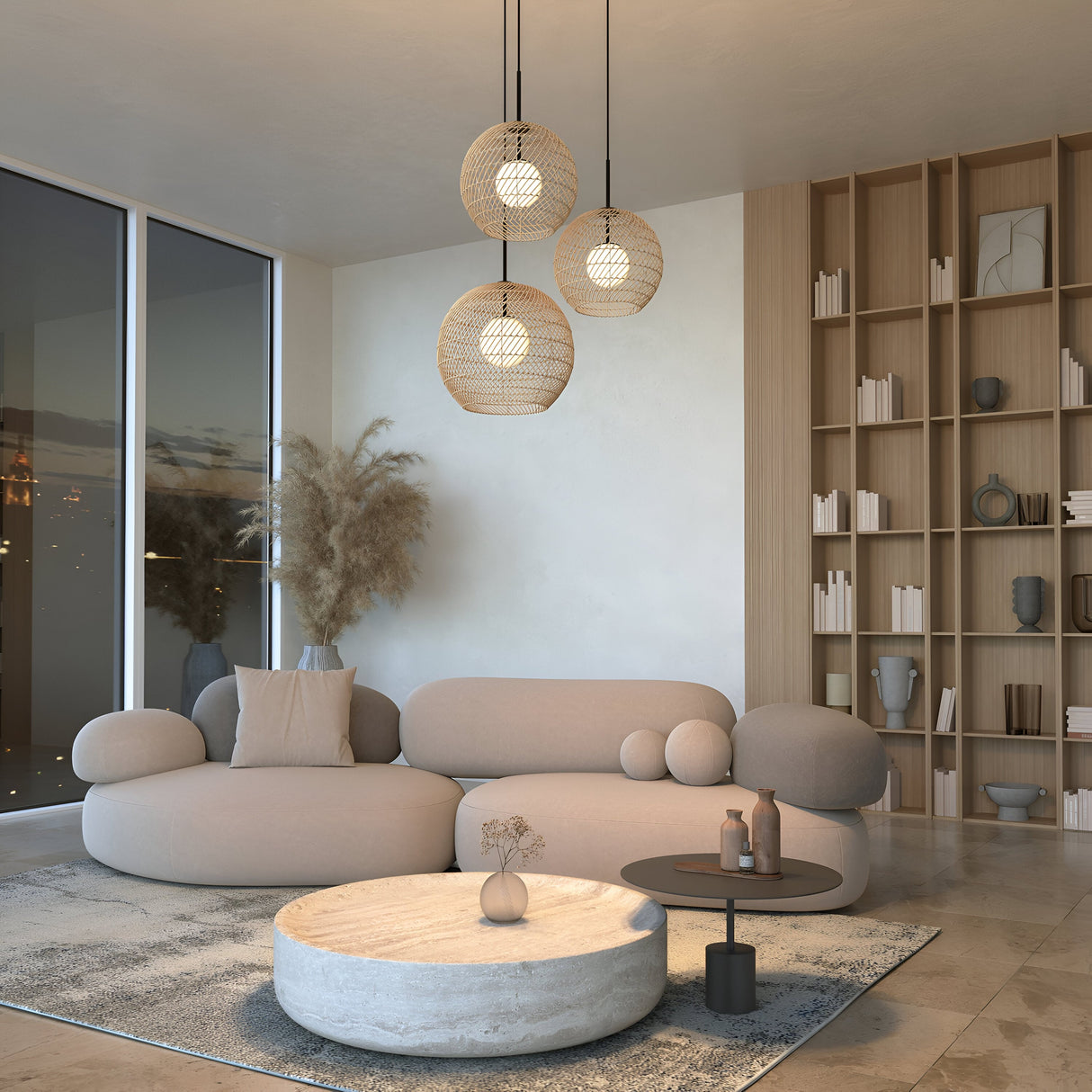 A modern living room features beige, rounded furniture and a circular coffee table. Three Cane Pendant Lights in black and beige wicker with white glass diffusers hang above. A textured rug, built-in shelves with books and decor, large windows, and dried plants in a vase contribute to the warmth.