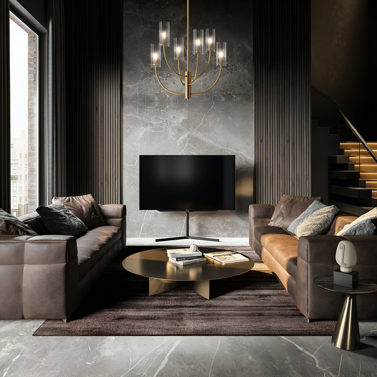 Two brown leather sofas face each other in a sophisticated living room. A large modern TV is mounted on a dark marble wall. A round coffee table with books stands at the center on a plush rug, while an elegant Arco 6 Light Chandelier - Brass with ribbed glass lampshades completes the decor.