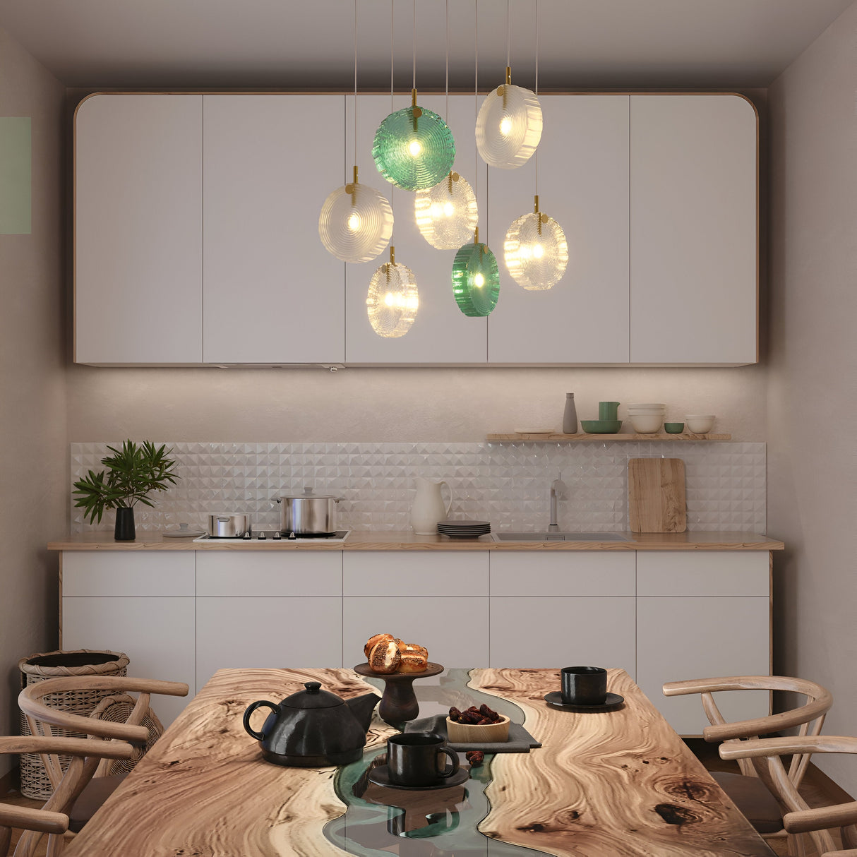 A modern kitchen showcases a wooden table with a blue resin river design. The Frozen 7 Light Cluster Pendant - Brass, along with other hanging lights, illuminates the space. In the background are white cabinets and a textured backsplash. On the table sit two black teacups and a teapot.