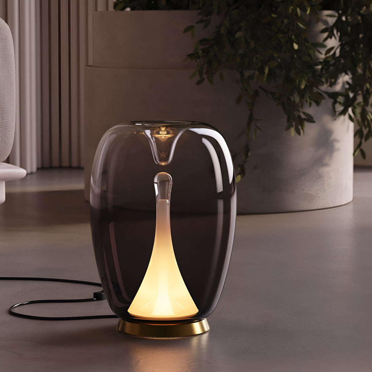A modern, translucent Splash LED Table Lamp 3000K 9W with a sleek Smoked Ombre Glass exterior and glowing gold interior stands on a smooth floor, accentuating a large potted plant and neutral-toned furniture.
