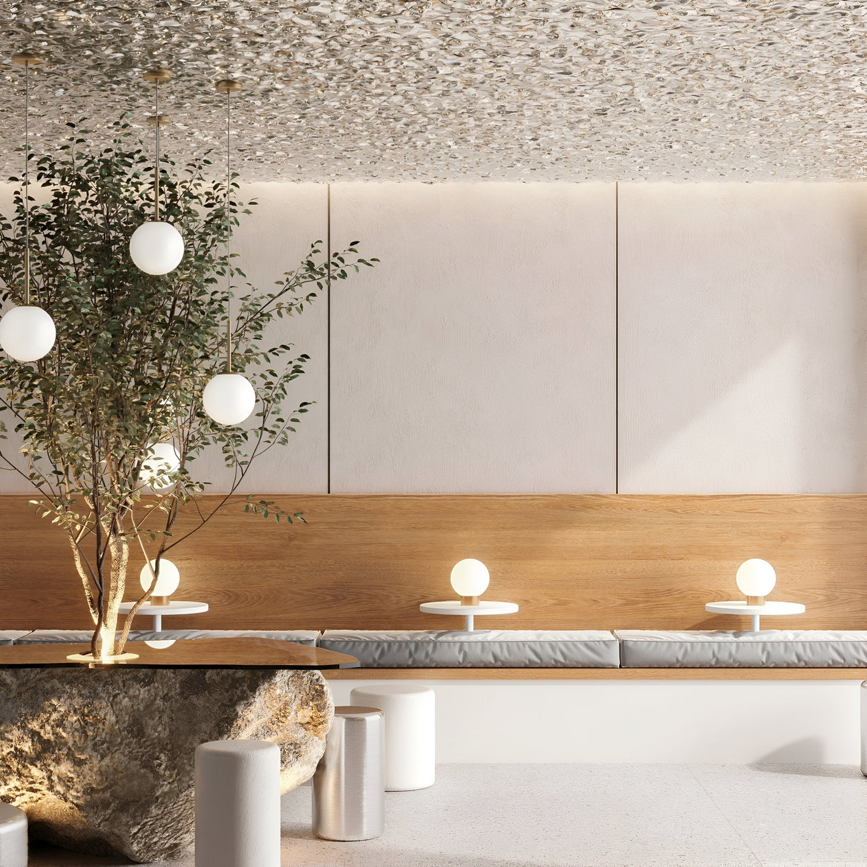 A modern interior with a natural design theme features a large rock table, cushioned benches, the Basic Form Table Lamp in gold with white frosted glass, small round tables with globe lamps, and a leafy tree. Beige and wood tones dominate the decor, enhanced by a textured ceiling.