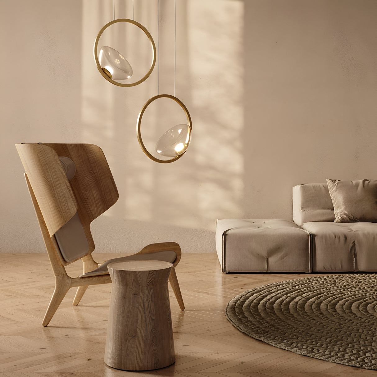A minimalist living room showcases a wooden chair, matching rounded stool, and beige tufted sofa. Two Lunare LED Single Ring Pendant Lights in brass with clear glass hang from the ceiling, while a textured round rug lies on the parquet floor, casting soft light shadows on the wall.