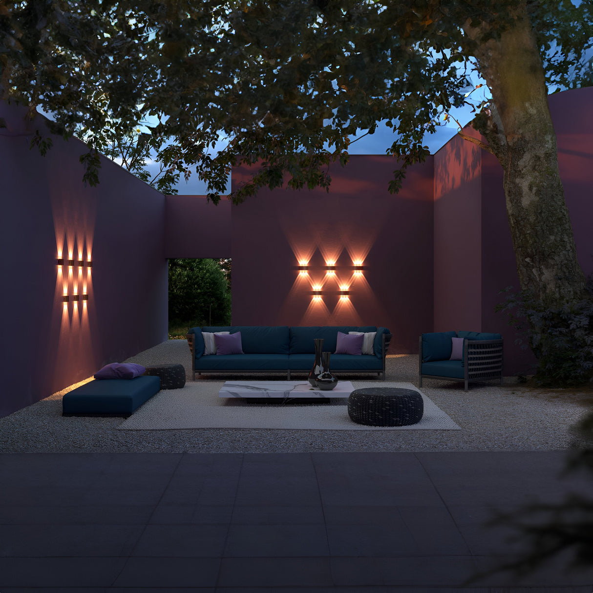 Outdoor patio with purple walls, modern teal sofa, chairs, and low table. Strato Outdoor LED Wall Light creates geometric patterns. A large tree provides partial shade as the evening sky looms above.