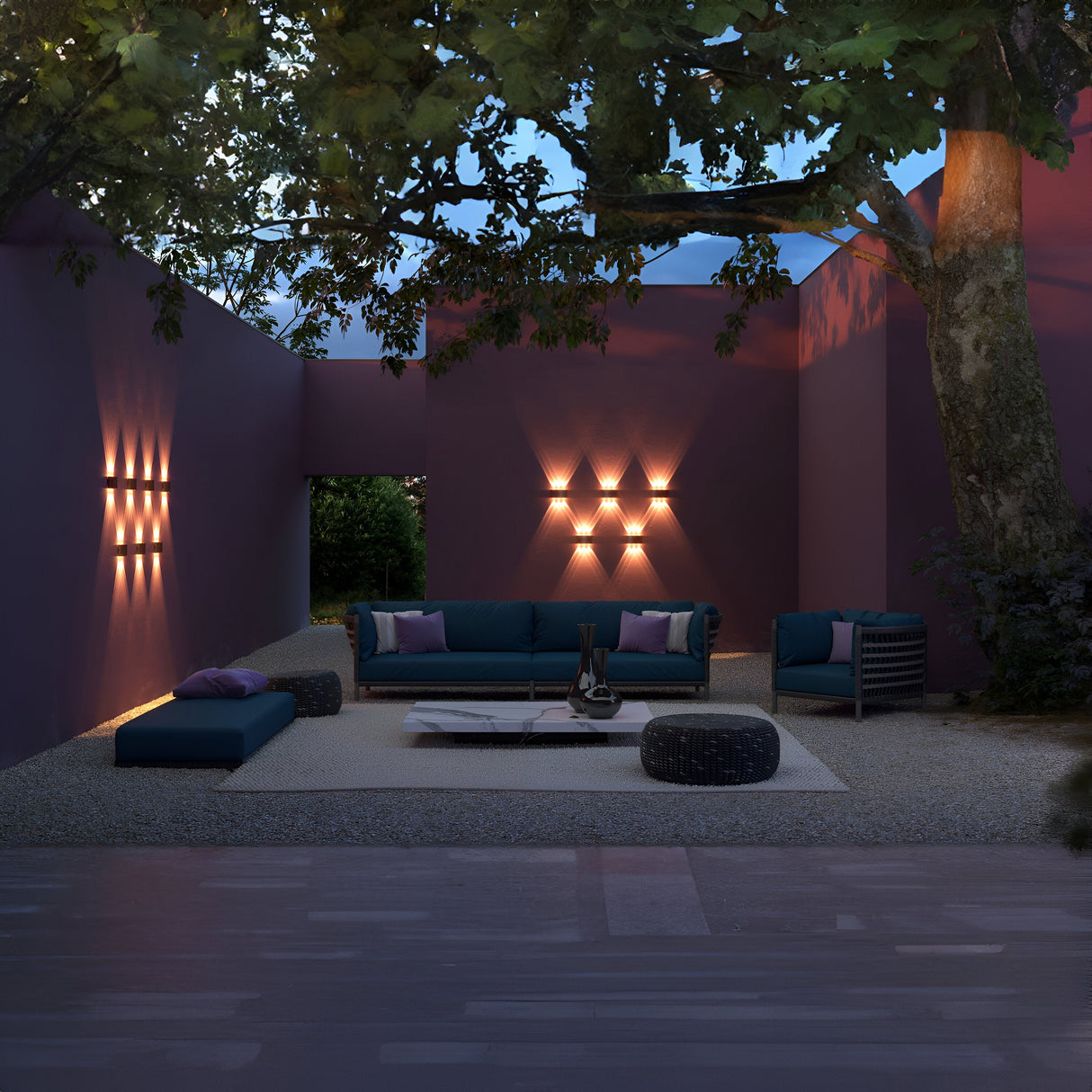The outdoor area boasts modern furniture, including a blue sofa and chair. A large tree covers the space with purple walls, accented by Strato Outdoor LED Wall Lights (6W, 3000K, IP54) in white, creating a warm ambiance over the gravel floor.