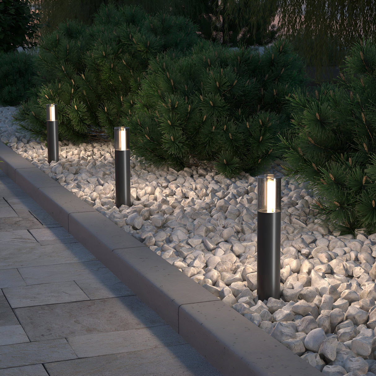 Four Glide Outdoor Long Spike Lights in graphite illuminate a garden area with pristine white stones and vibrant green shrubs, casting a warm glow that highlights the immaculate landscaping along a paved walkway.