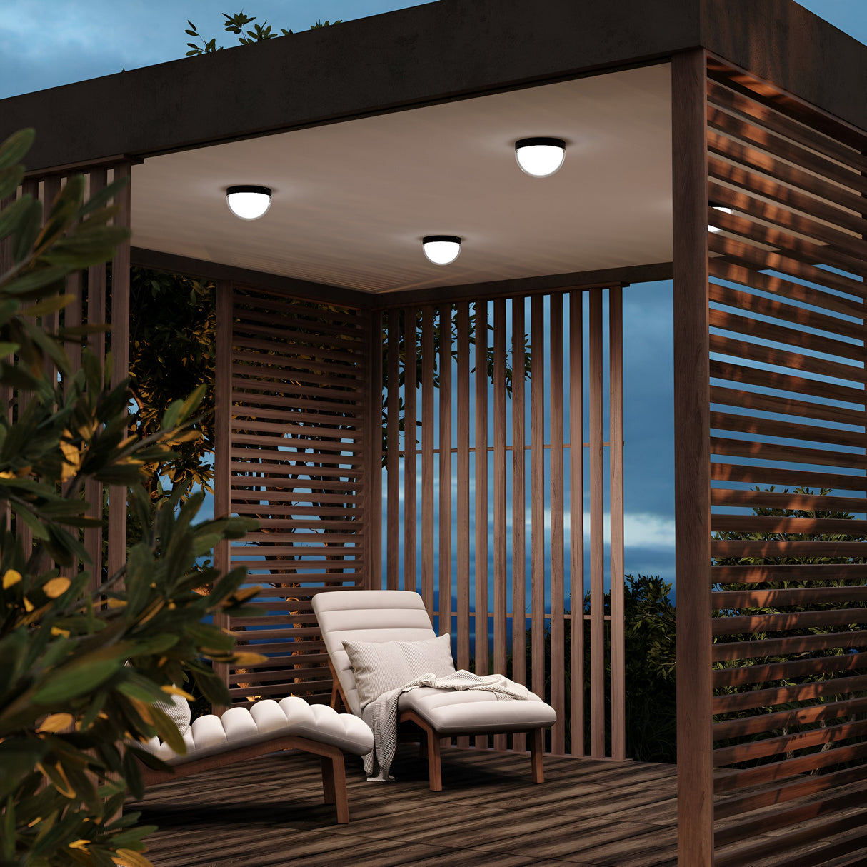 A modern outdoor gazebo features slatted wooden walls with a graphite finish and is enhanced by the Mon Outdoor LED Ceiling Light 3000K. Inside, a white cushioned lounge chair and small side table embrace the tree-surrounded setting as the overcast sky crafts a serene evening.