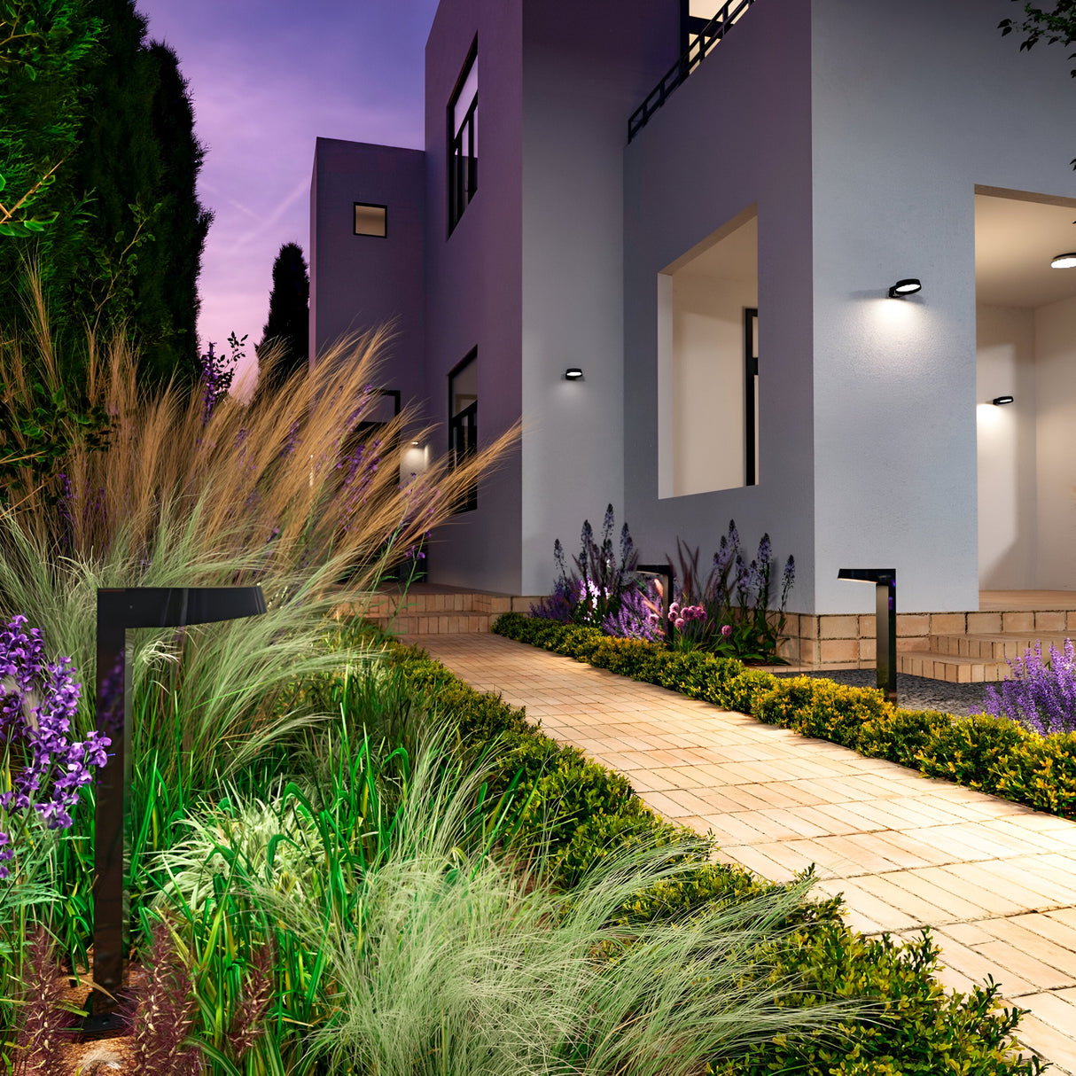Modern buildings with large windows light up at dusk, featuring paths lined with greenery and purple flowers illuminated by sleek Share LED Bollard Light 65cm in Graphite. The sky’s purple and pink gradient beautifully complements the tranquil landscaped outdoor spaces.