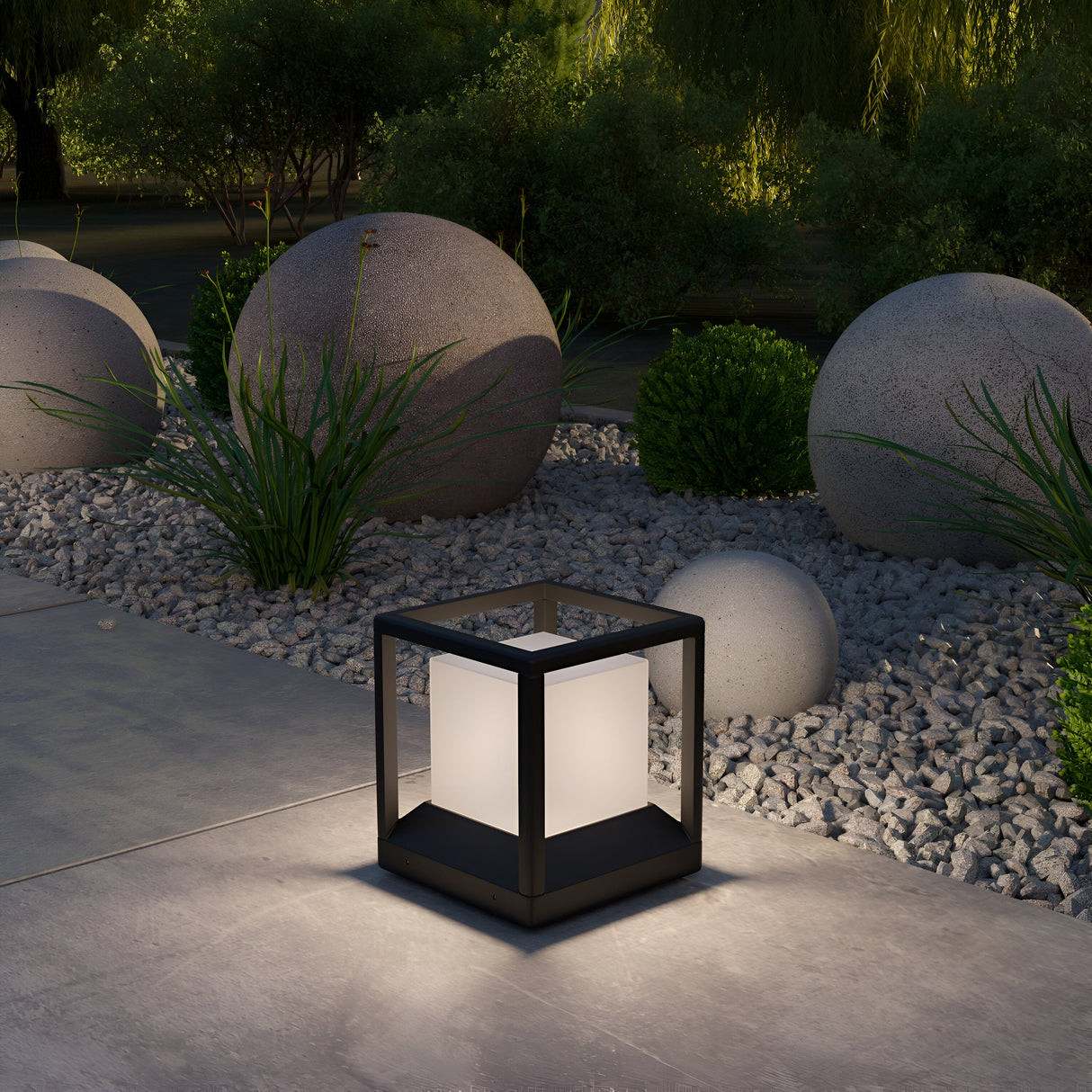 The Trim Pedestal Light 255mm in graphite illuminates a garden at dusk, complementing spherical stone decorations, small shrubs, and gravel for a minimalist and serene atmosphere.