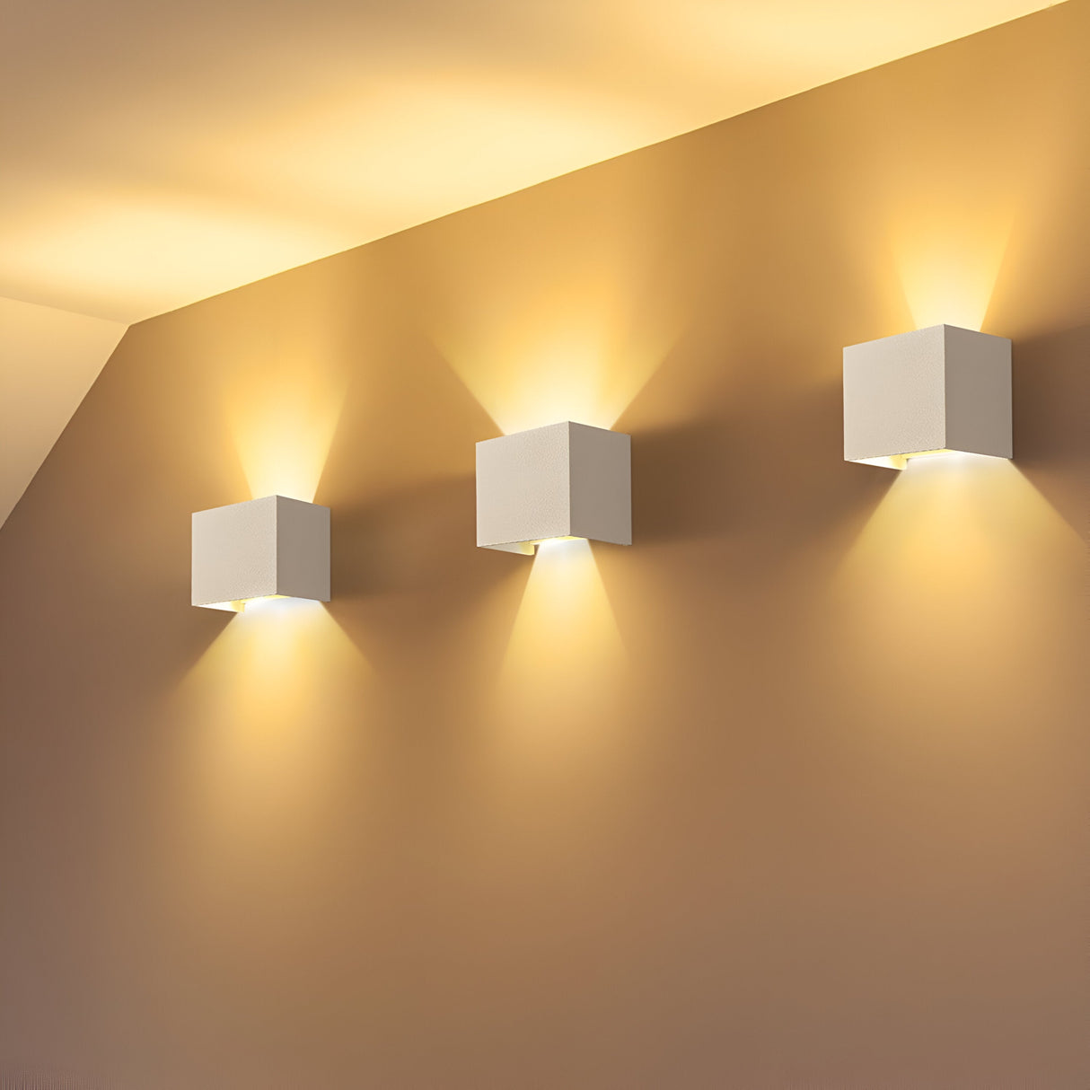 Three Fulton Outdoor LED Rectangular Wall Lights, crafted from corrosion-resistant aluminum, illuminate a beige wall both upward and downward. Their energy-efficient modules create a warm glow, delivering a modern and cozy ambiance.