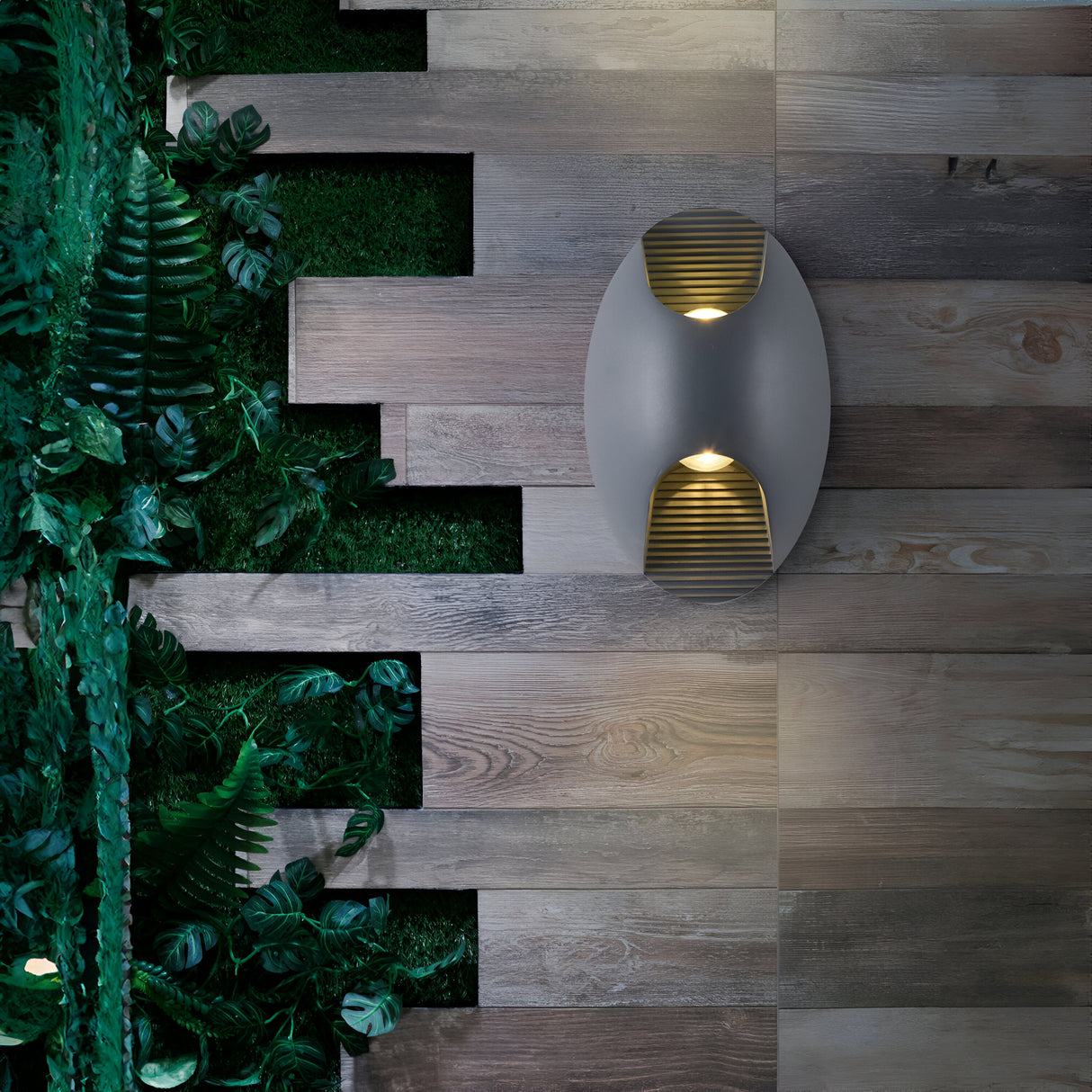 The Times Square Outdoor Wall Light 3000K 6W - White casts a soft glow on the wood-paneled wall. Lush green plants to the left create a vertical garden effect, beautifully contrasting with the smooth wood texture, combining natural and contemporary elements in this energy-efficient design.