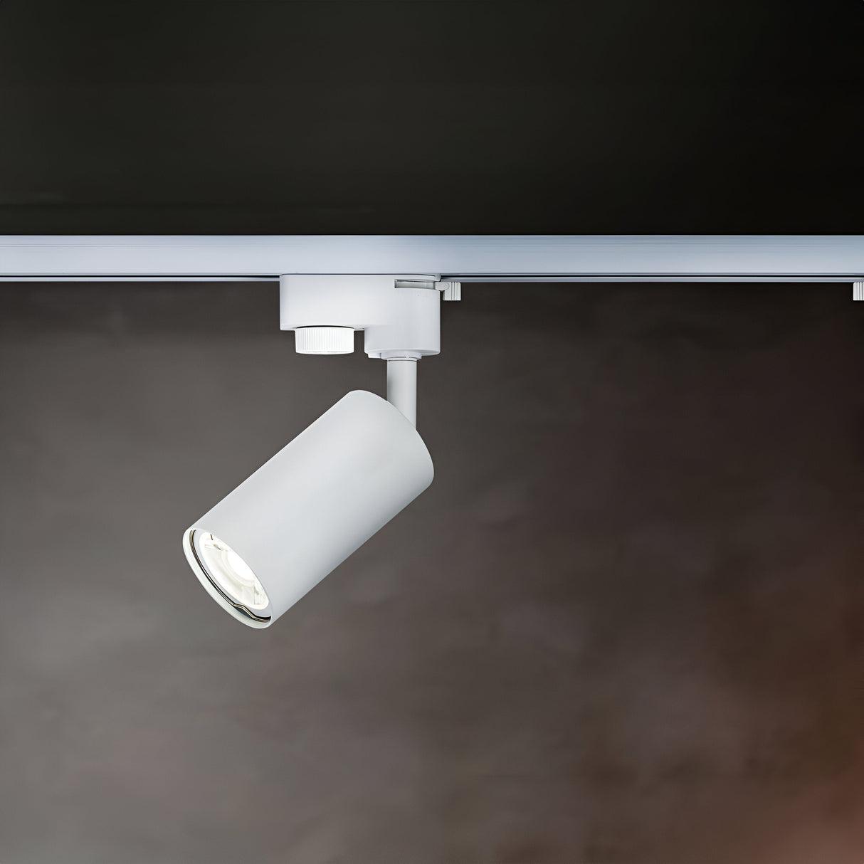 A close-up of the white Focus Mini Single Phase Unity Track Spotlight against a dark background shows the cylindrical light attached to a horizontal track, angled downward for accent lighting.