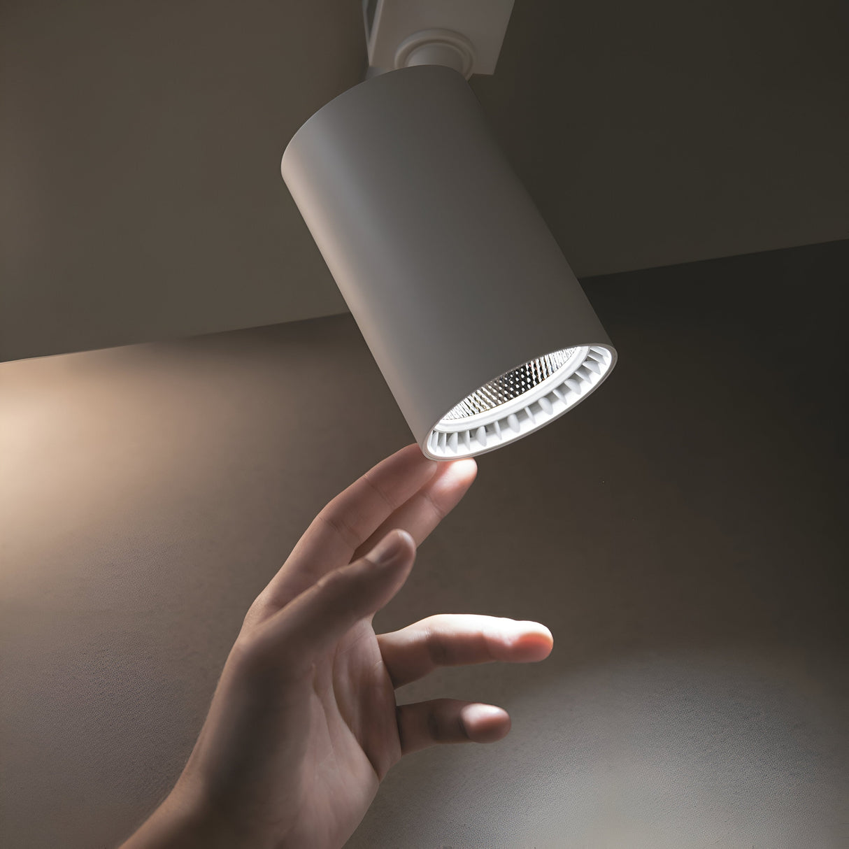 A hand reaching for a Vuoro S LED Single Phase Unity Track Spotlight 15W 3000K in white, emitting soft shadows on the wall in a dimly lit space, highlights its high CRI interaction.