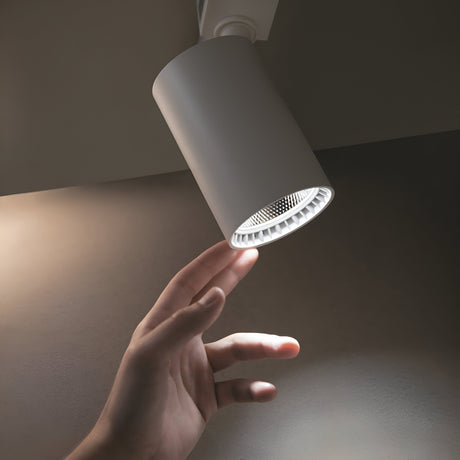A hand reaching for a Vuoro S LED Single Phase Unity Track Spotlight 15W 3000K in white, emitting soft shadows on the wall in a dimly lit space, highlights its high CRI interaction.