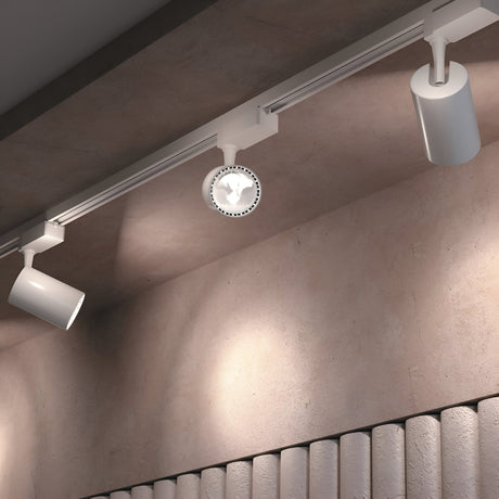 A ceiling-mounted track lighting system with two cylindrical fixtures and a Vuoro LED Single Phase Unity Track Spotlight 26W 4000K in white illuminates a textured beige wall, casting gentle shadows, complemented by partially visible vertical panel details below.