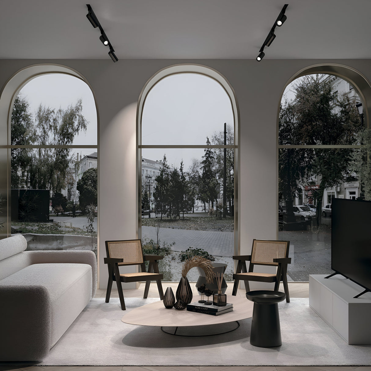 A modern living room with large arched windows overlooks a tree-lined street. It features a white sofa, wooden chairs, and a round coffee table adorned with decorative vases. The sleek TV on a stand is enhanced by the Focus Single Phase Unity Track Spotlight in black for visual comfort.