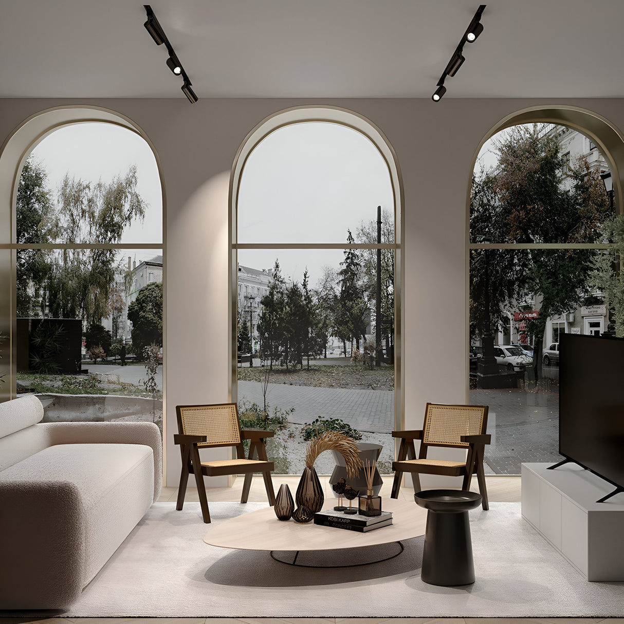 A modern living room with arched windows overlooks a tree-lined street, featuring a white sofa, two wooden chairs, and a round coffee table with decor. A large flat-screen TV and Focus Single Phase Unity Track Spotlight in graphite add elegance for optimal GU10 bulb compatibility.