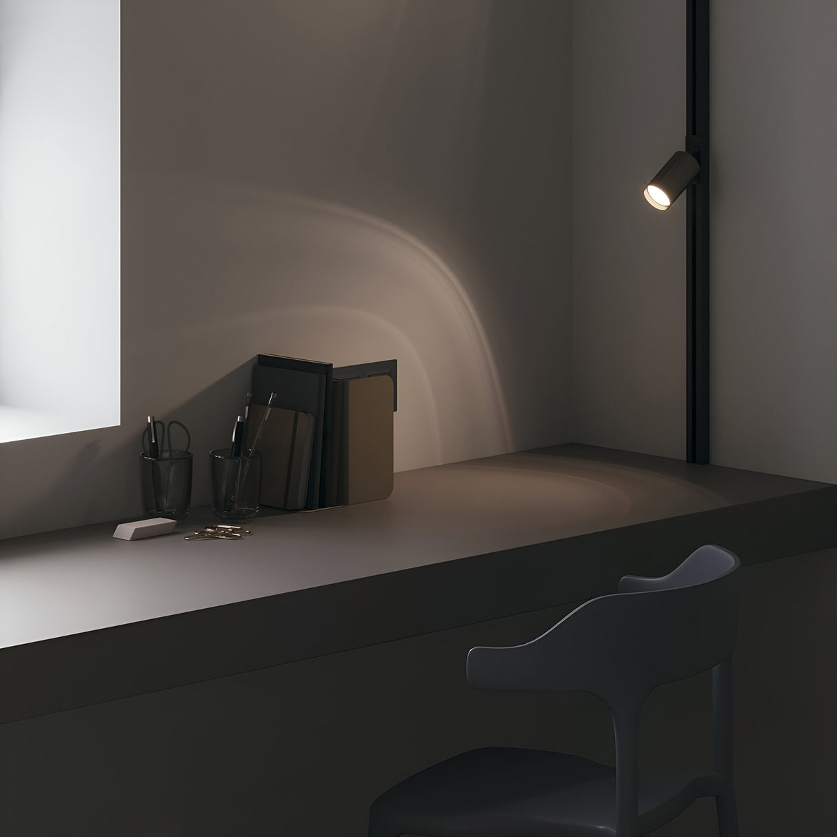 A modern workspace showcases a sleek grey desk paired with a black chair. The desk bears a few organized black folders, two glasses filled with pens, and a small notepad. The Focus Single Phase Unity Track Spotlight in matte gold elegantly illuminates the scene with GU10 compatibility for superior lighting.