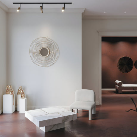 Modern living room with a minimalist design featuring a white armchair and geometric marble table. A large, circular wall decoration and two bronze sculptures accent the space. The black & gold Elti Single Phase Unity Track Spotlight illuminates the area, enhancing the ambiance perfectly.