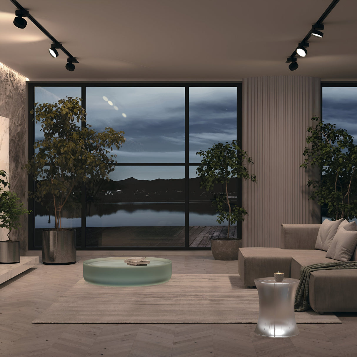 A modern living room with large windows showcasing a lake view at dusk is elegantly lit by Onda LED Single Phase Unity Track Spotlight 18W 4000K - Black. The space features a beige L-shaped sofa, transparent circular coffee table, small side table, and potted plants on a light wood floor.