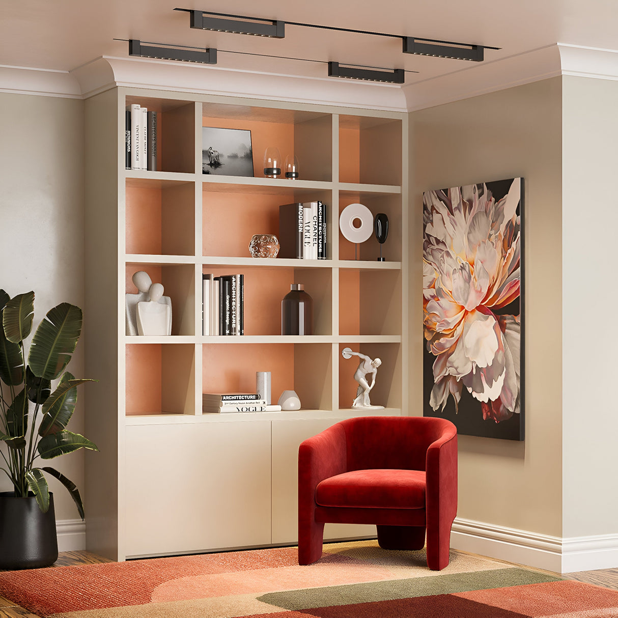 A cozy room features a large bookshelf with books and decor, a red velvet chair illuminated by a Points Rot LED Swivel Linear Track Light in matte black. A colorful floral painting adorns the wall, while a large potted plant rests on a patterned rug in the corner.