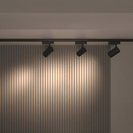 A modern interior with ceiling-mounted Vuoro 3-Circuit Trinity Track LED Spotlights in black (26W, 3000K) showcases a vertical slatted gray wall. These high CRI lights create a warm ambiance, highlighting the walls texture.