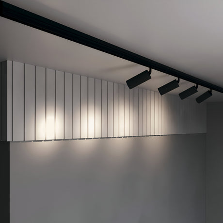 A ceiling features energy-efficient recessed lights and a row of Focus LED Magnetic Exility Track Spotlight 20W 3000K - Black. The wall below, with vertical panels, is elegantly lit to create a sleek and contemporary atmosphere.