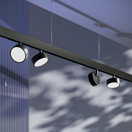The Rado LED Magnetic Exility Track Spotlight 18W 4000K - Black, a modern fixture with four circular lights, hangs from the ceiling. It uses energy-efficient lighting and casts soft, dappled shadows through its translucent textured panel for a calming minimalist aesthetic.