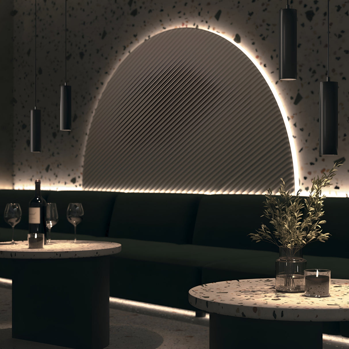 A modern, dimly lit lounge features a geometric light installation and the sleek Focus LED Exility Magnetic Track Pendant Light in black. Two round terrazzo tables hold wine glasses, a wine bottle, and a potted plant, capturing the essence of modern industrial style perfectly.