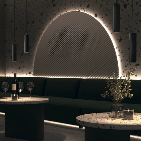 A modern, dimly lit lounge features a geometric light installation and the sleek Focus LED Exility Magnetic Track Pendant Light in black. Two round terrazzo tables hold wine glasses, a wine bottle, and a potted plant, capturing the essence of modern industrial style perfectly.