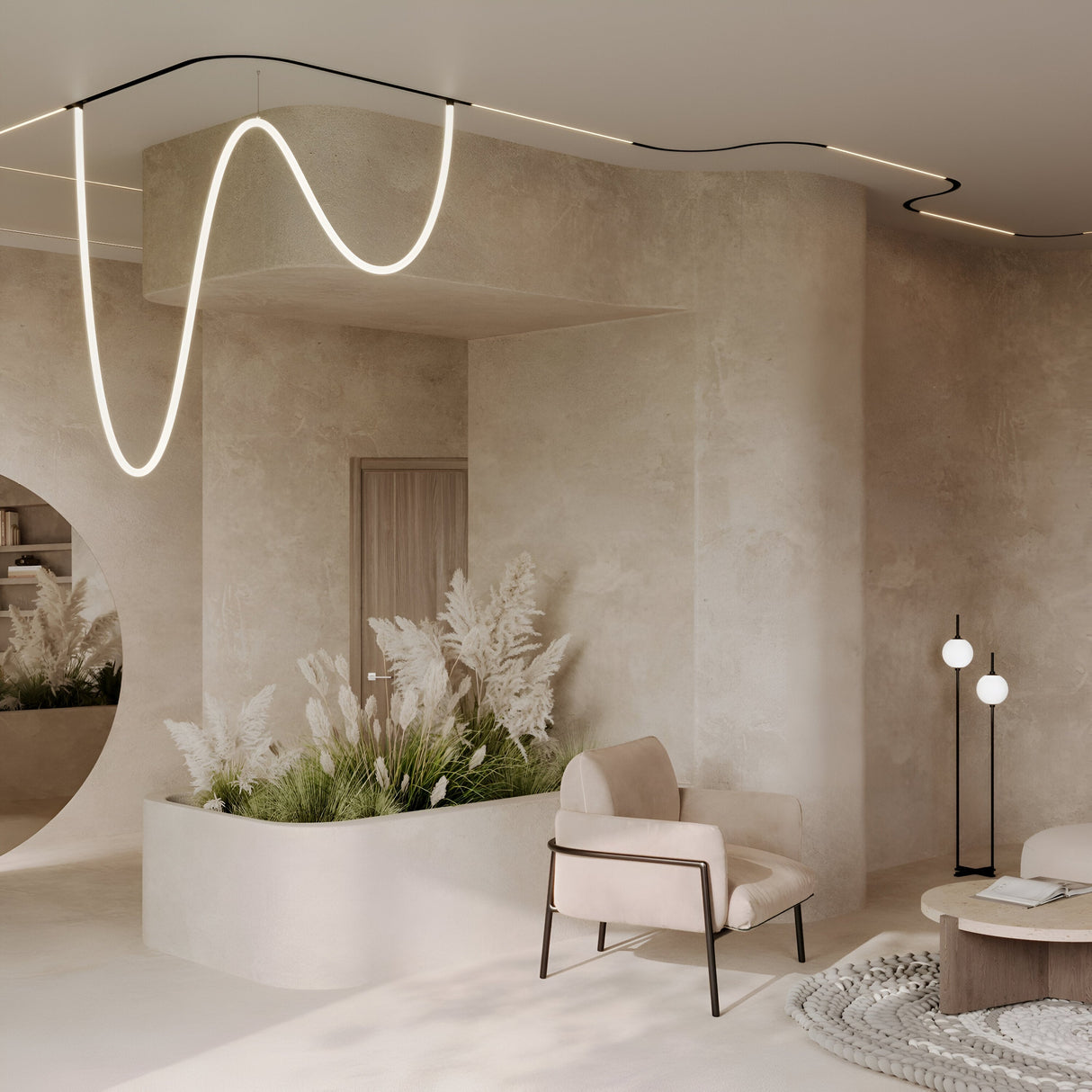 A minimalist room features beige walls, an abstract ceiling light, and Exility Tracks Radius Connector R300 recessed track lighting. A light beige armchair, a small round wooden table, pampas grass in a planter, and a modern floor lamp accompany the space. A large round mirror adds reflection.