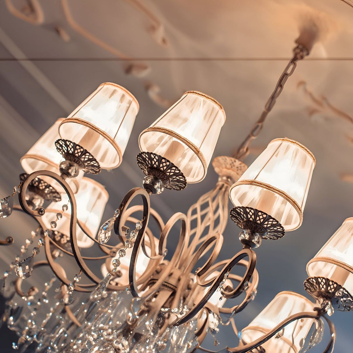 The Grace 10 Light Chandelier - White exhibits intricate metalwork and multiple lampshades, embellished with crystal pendants for a luxurious feel. The chandeliers soft top illumination beautifully highlights its detailed design.