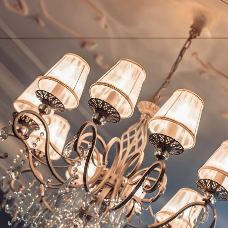 The Grace 10 Light Chandelier - White exhibits intricate metalwork and multiple lampshades, embellished with crystal pendants for a luxurious feel. The chandeliers soft top illumination beautifully highlights its detailed design.