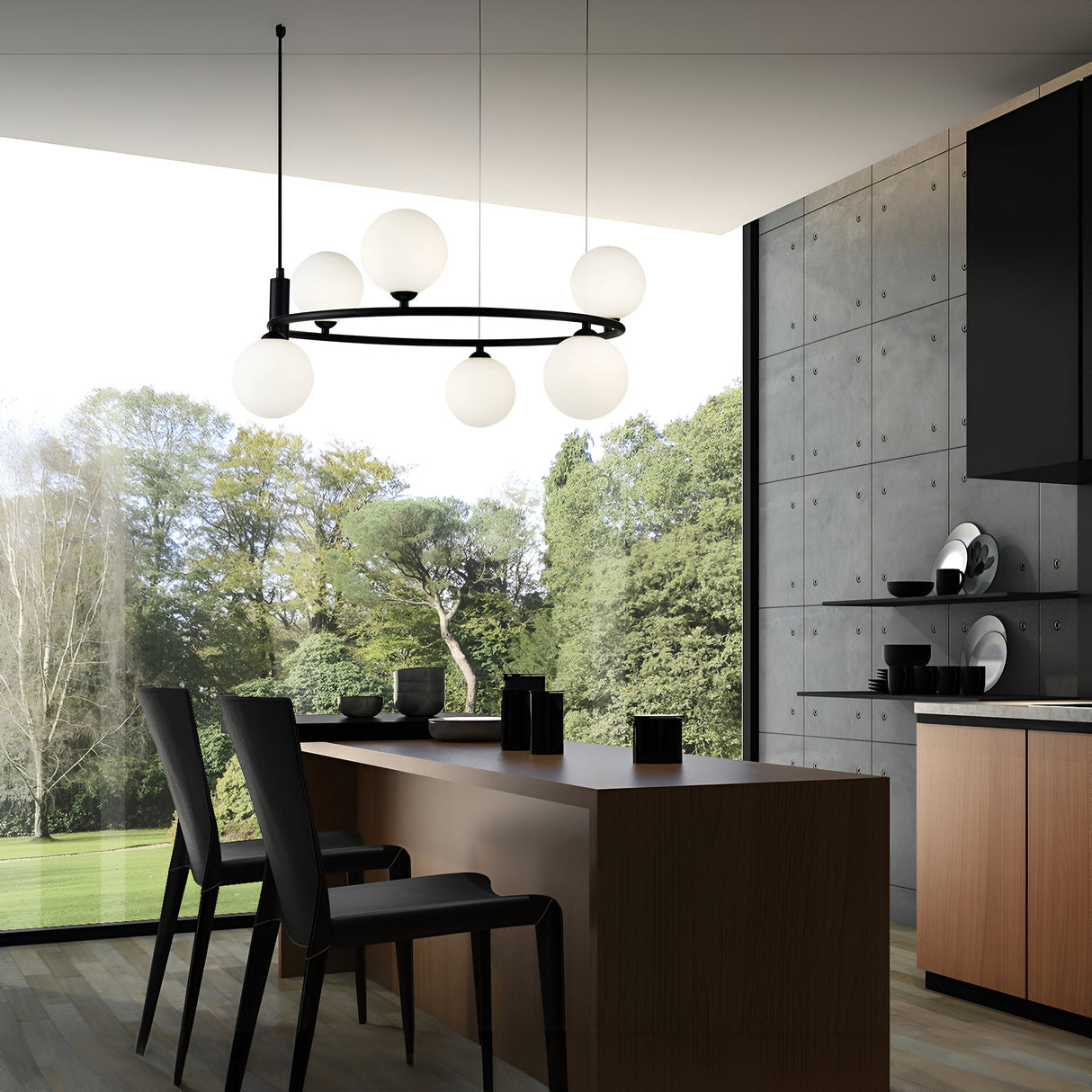 A modern dining area features a wooden table and black chairs under the elegant Ring 6 Light Circular Suspension in black with six frosted white glass spheres. Large windows showcase lush green trees and a neat lawn, while a minimalist kitchen lies to the right.
