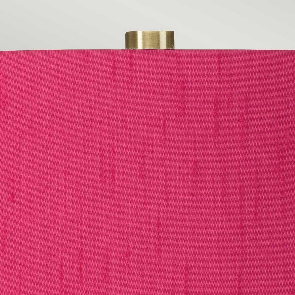 Close-up view of the Isla 1 Light Table Light - White/Pink, featuring a bright pink textured fabric shade with a small cylindrical brass fitting at the top, set against a neutral background.
