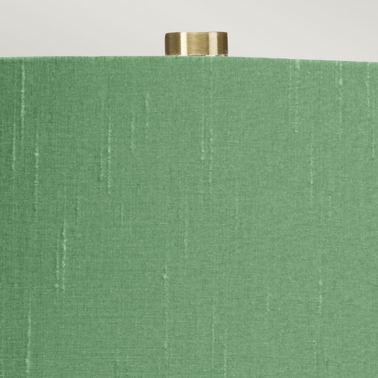 The Isla 1 Light Table Light - White/Green is captured in a close-up that highlights its textured green shade accented with subtle vertical stripes and topped with a small brass finial. Placed against a neutral backdrop, this lamp pairs elegantly with its white ceramic base, blending sophistication with an understated design.
