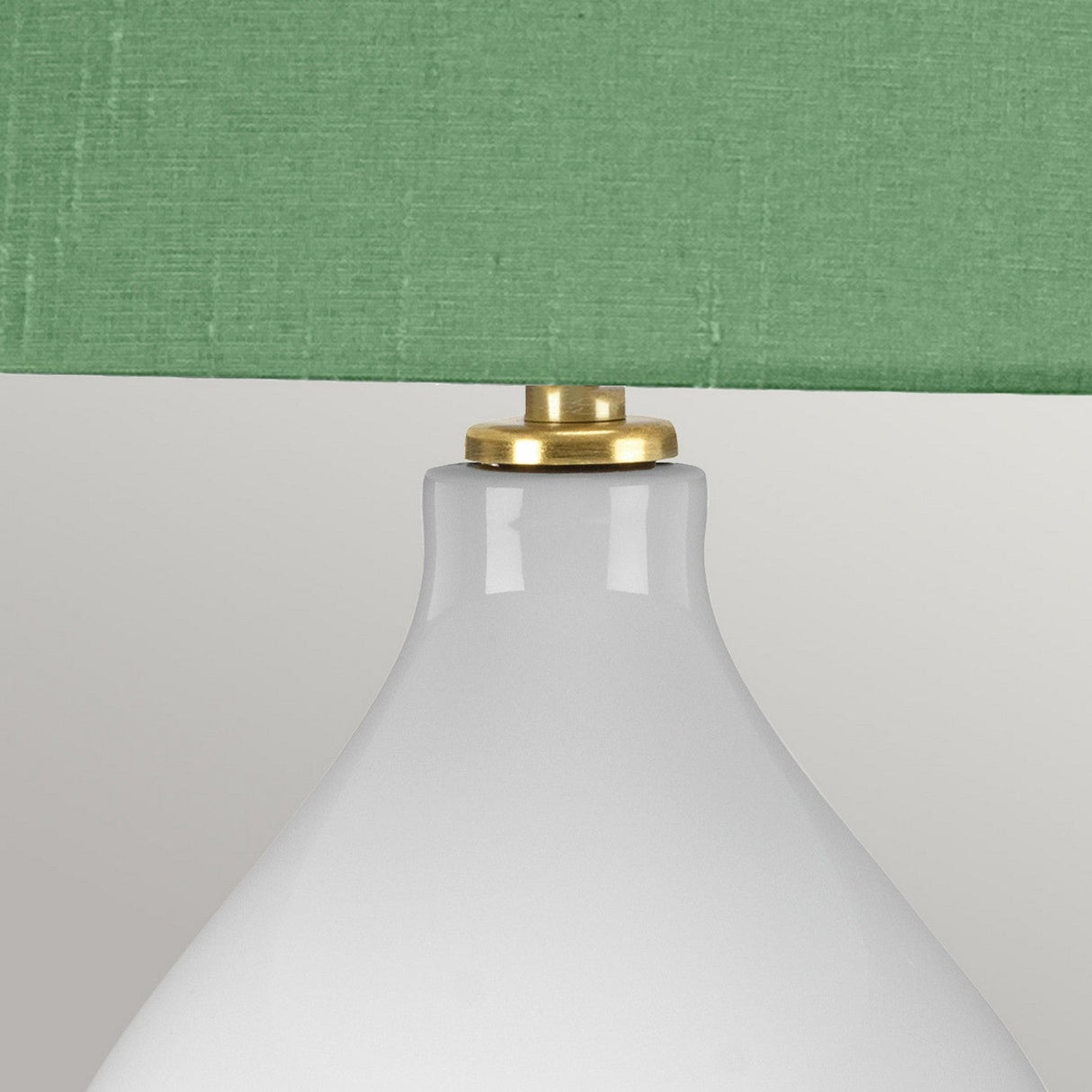 A close-up of the Isla 1 Light Table Light - White/Green showcases its white ceramic base paired with a green fabric lampshade, elegantly divided by a brass ring.
