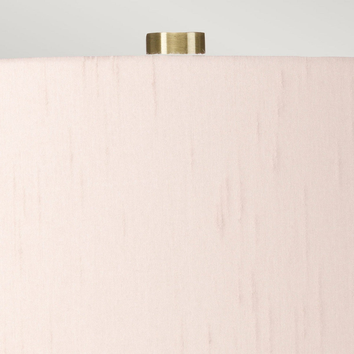 Close-up of the upper section of a cylindrical beige lampshade with a smooth texture. A small, metallic, cylindrical finial is prominently visible at the top against a light gray background, seamlessly enhancing the elegance of the Isla 1 Light Table Light - White/Light Pink ceramic base lamp.