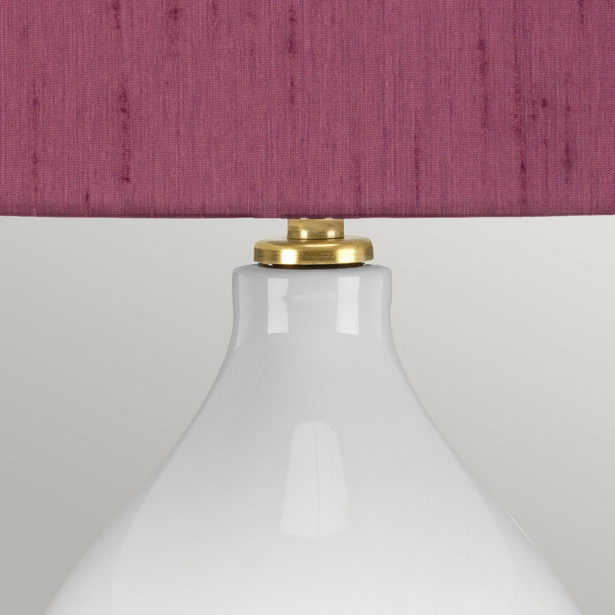A close-up of the Isla 1 Light Table Light showcases its ceramic base with a brass accent, complemented by a textured purple shade. The background features a soft gray tone.