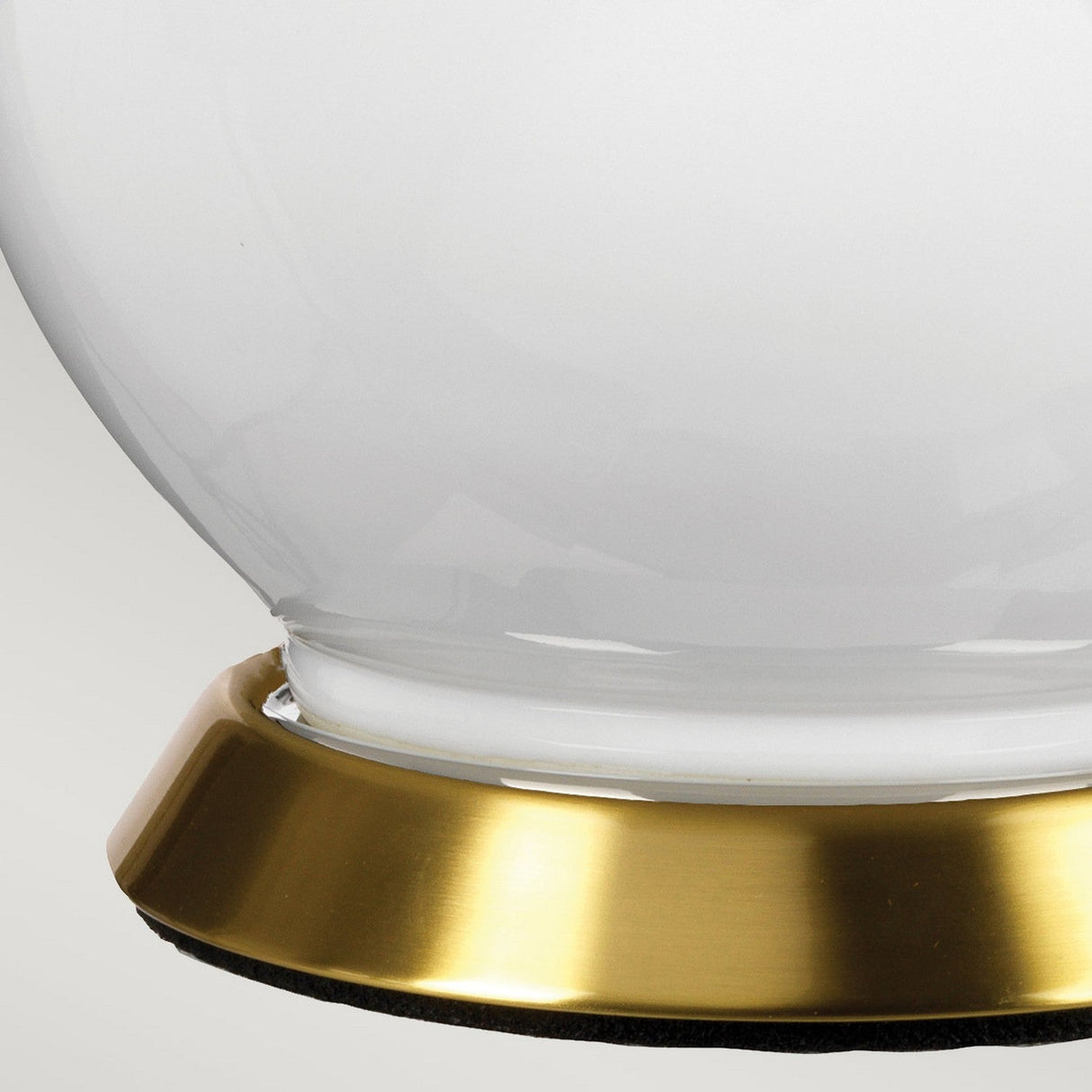 A close-up of the Isla 1 Light Table Light in white and purple shows its glossy ceramic surface with a shiny gold-colored base, casting a soft purple glow on the light gray background.