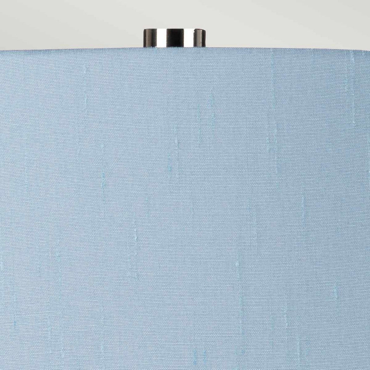 Close-up view of the Isla 1 Light Table Light, featuring a light blue textured lampshade with a small metallic knob on top, resting on a ceramic base, set against a light gray background.