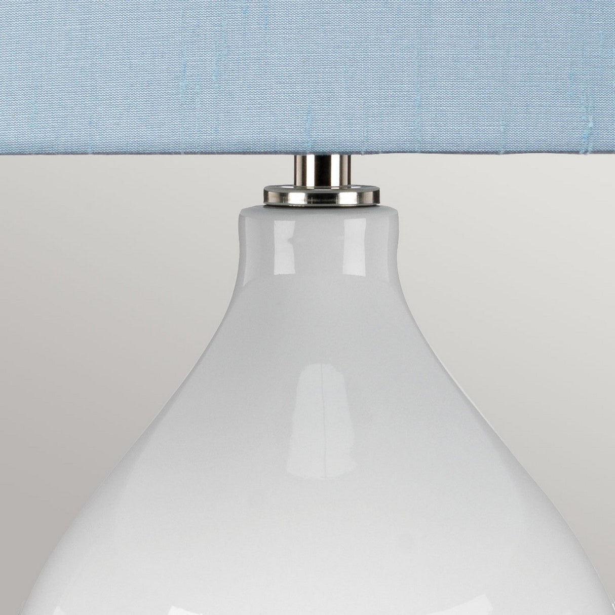 A close-up of the Isla 1 Light Table Light - White/Blue highlights its glossy white ceramic base and light blue fabric shade, complemented by a sleek silver fixture connecting the base and shade.