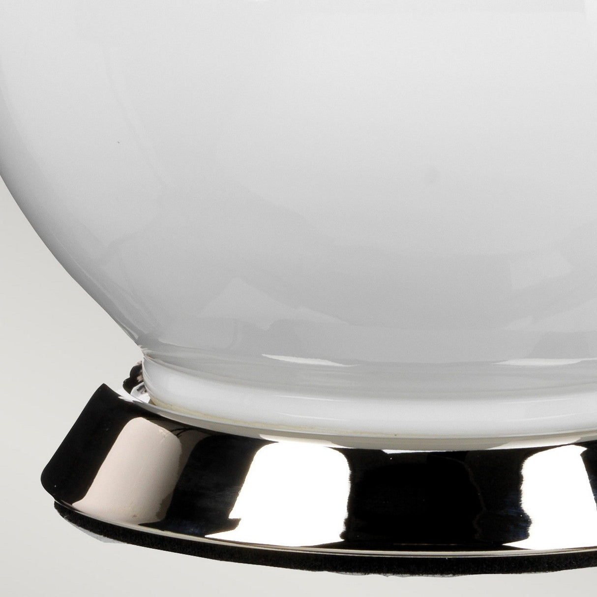 Close-up of the Isla 1 Light Table Light in White/Blue, featuring a shiny, reflective metallic base supporting a smooth, glossy white component. The background is softly blurred, emphasizing the table light's elegant curves and metallic luster.