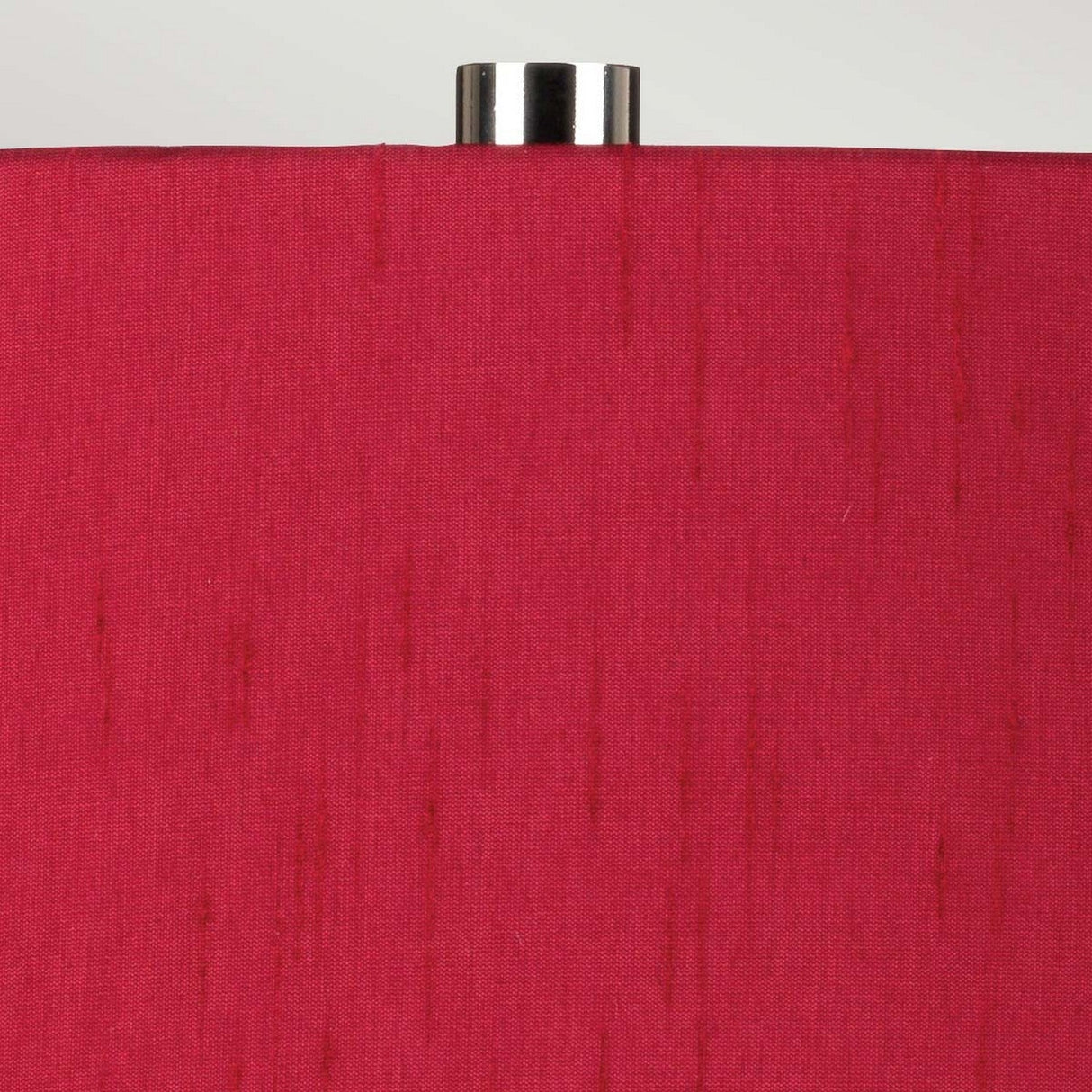 Close-up of the Isla 1 Light Table Light, showcasing a red fabric shade embellished with vertical thread patterns. Its white ceramic base harmonizes beautifully with the vibrant shade, and it is elegantly topped with a silver metal finial, all against a simple light gray background.