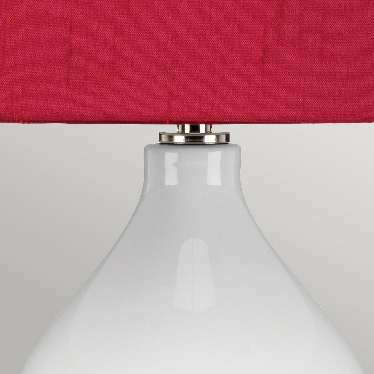A close-up of the Isla 1 Light Table Light showcases a white ceramic base with a smooth, glossy finish. It features a red fabric shade with a subtle texture, all set against a plain, light gray background.