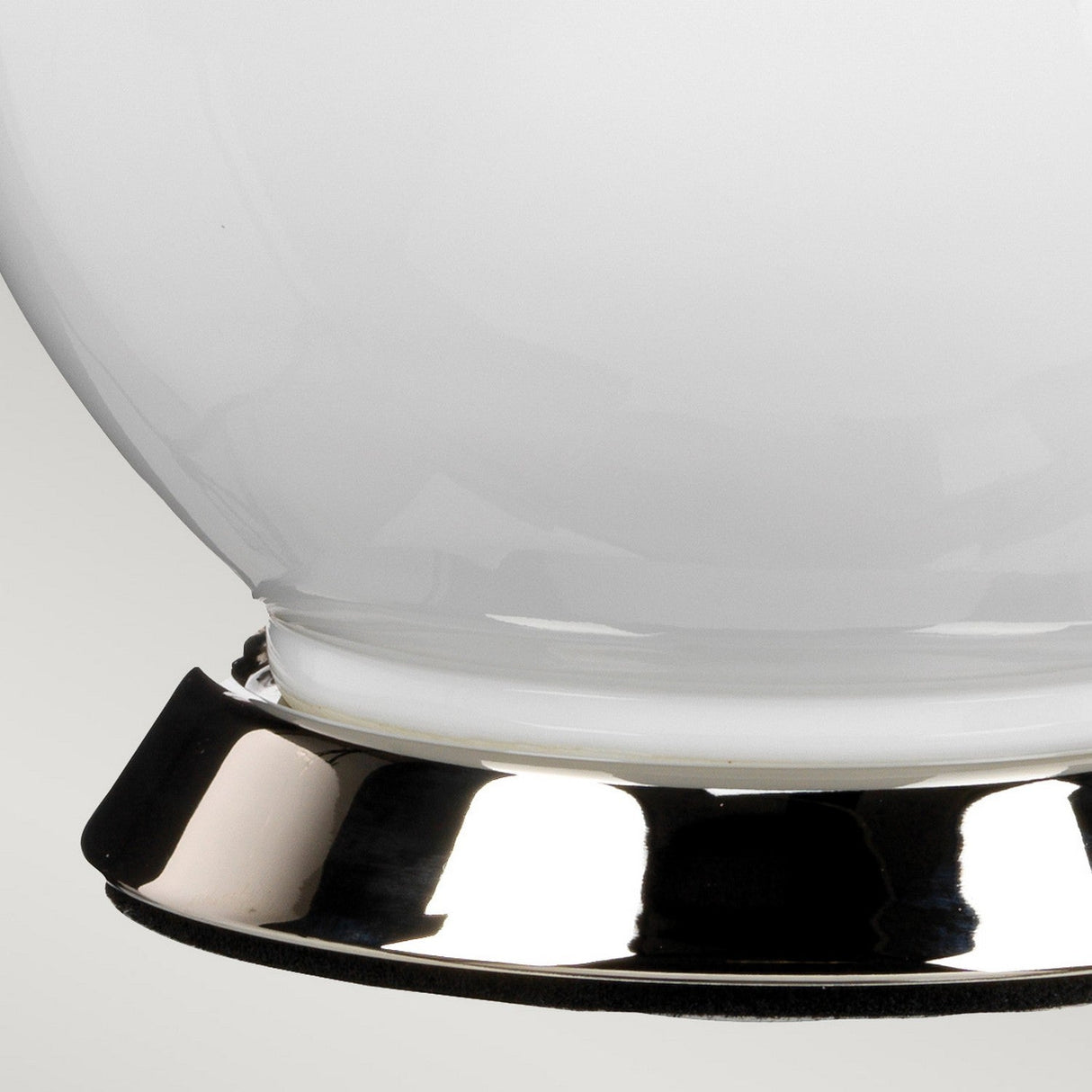 The Isla 1 Light Table Light in White/Red features a shiny metallic base supporting its sleek glass design. The surface brilliantly reflects light, accentuating the smooth curves and reflective quality of the metal. The glossy glass contrasts beautifully with the polished metal base, creating an elegant interplay of textures and luminosity.