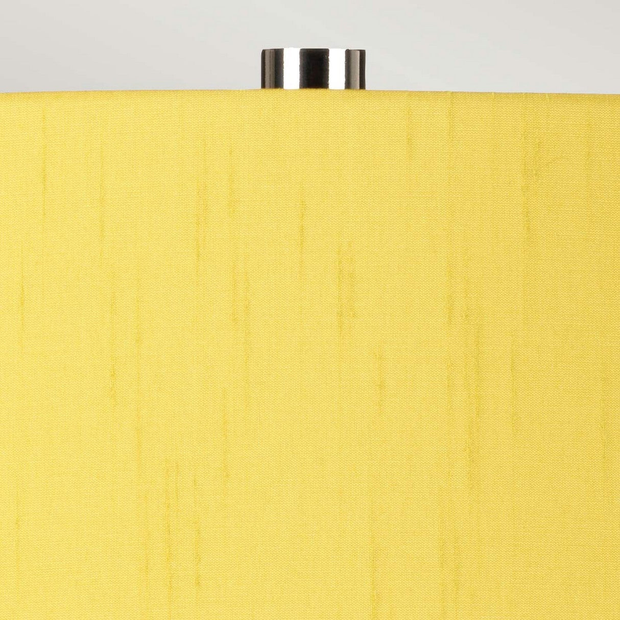 Close-up of the Isla 1 Light Table Light in White/Yellow, showcasing its yellow shade with a smooth texture and silver top, perfectly paired with a sleek ceramic base. The backdrop is a soft grayish color.