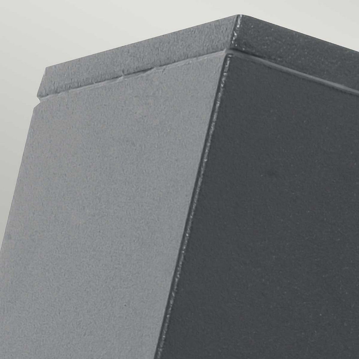 Close-up of the corner of a textured, rectangular graphite structure against a light gray background. The image captures the angular design and smooth surface of this Jannik 1 Light Outdoor LED Wall Light, highlighting its energy-efficient lighting and IP44 rating.