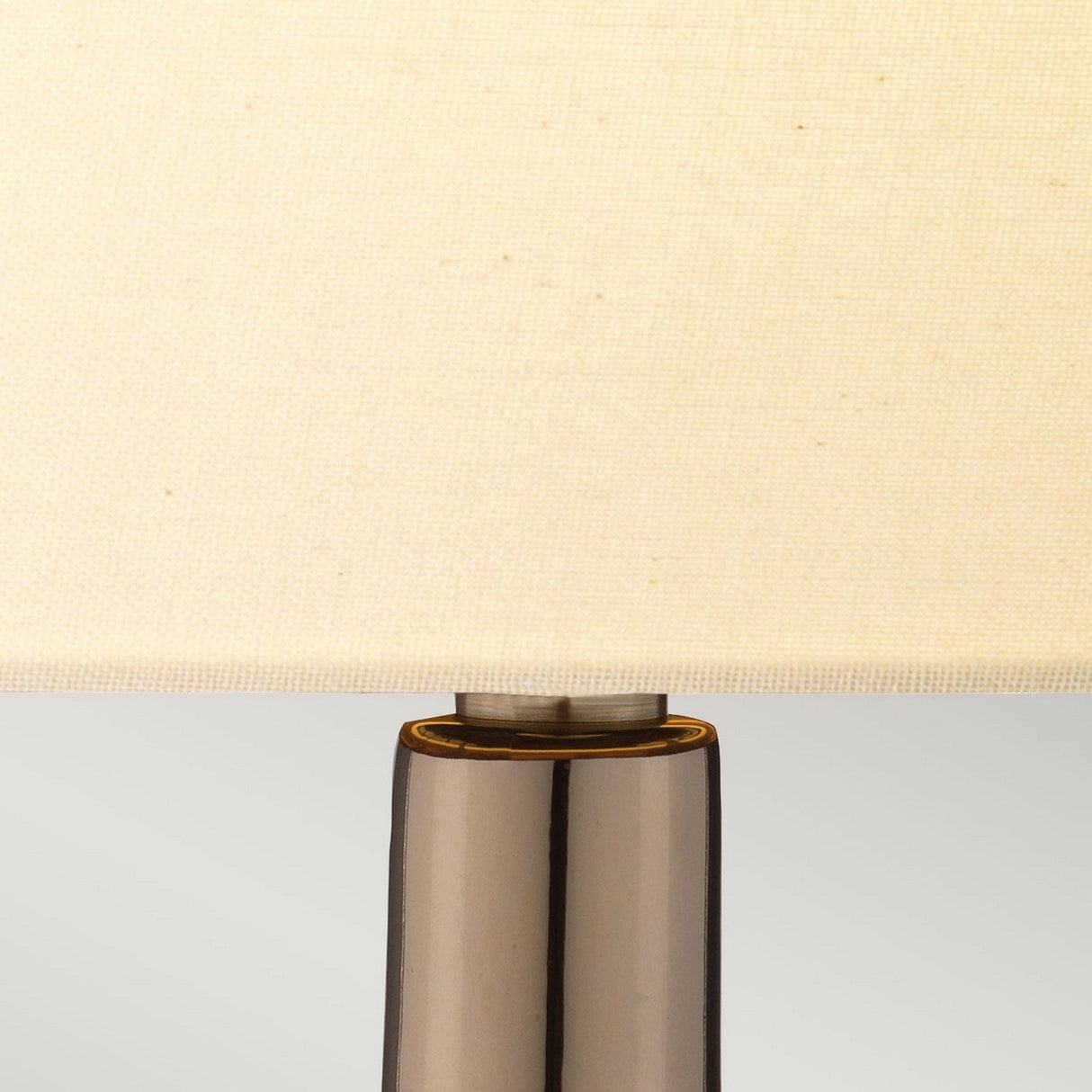 Close-up of the Job 1 Light Table Lamp, showcasing its cream faux silk shade set upon a glossy bronze metallic base. The light gray background highlights the lamp’s sleek and minimalist design.