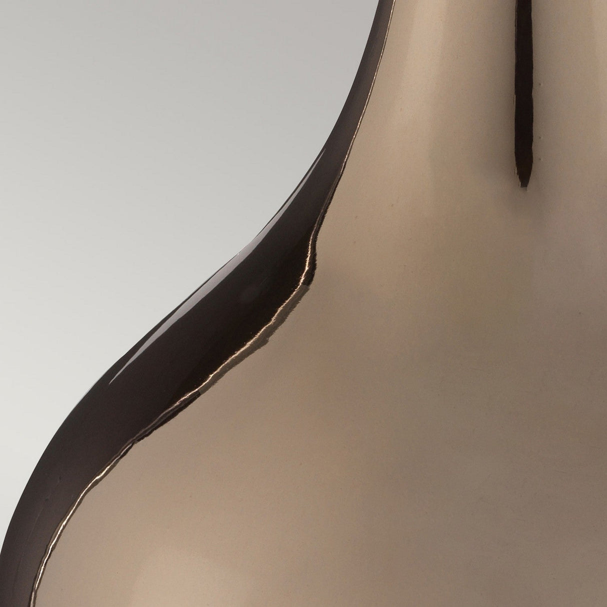 A close-up of the Job 1 Light Table Lamp in bronze metallic showcases its sleek, glossy finish with smooth curves and a reflective surface, set against a neutral gray background. The lamp features a modern, abstract shape that exudes elegance and simplicity.