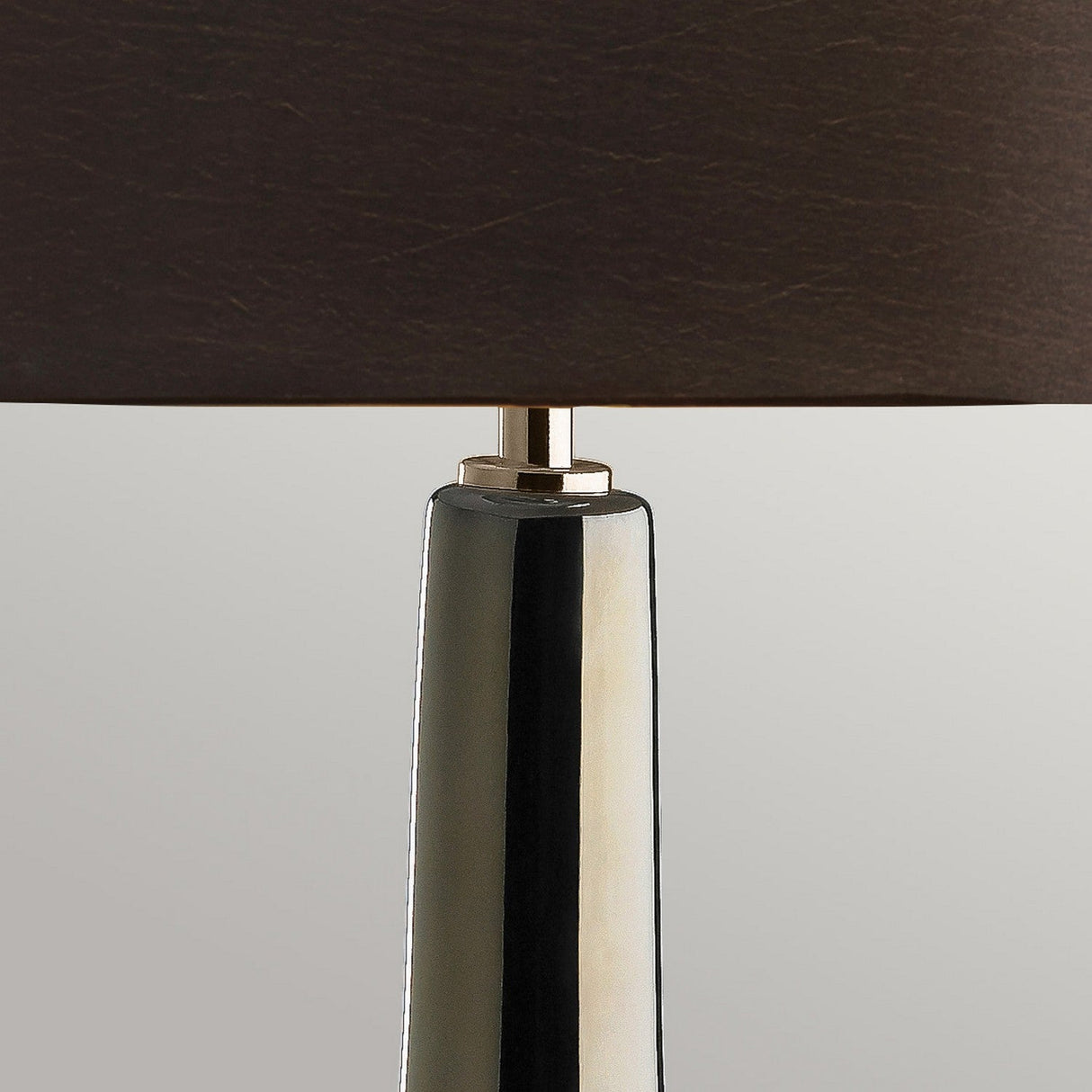 A close-up of the Job 1 Light Table Lamp, showcasing its modern ceramic base with a sleek bronze metallic and brown finish, complemented by a dark faux silk shade. The glossy design stands out elegantly against a neutral gray background.